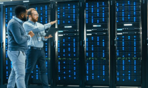 Two male technicians with a laptop, pointing at a switch in a server room