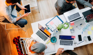 Looking down on an office desk littered with laptops and devices