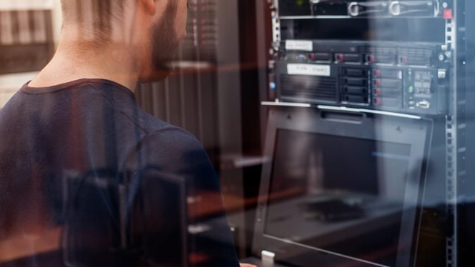 Developer sitting in front of computer with server in background