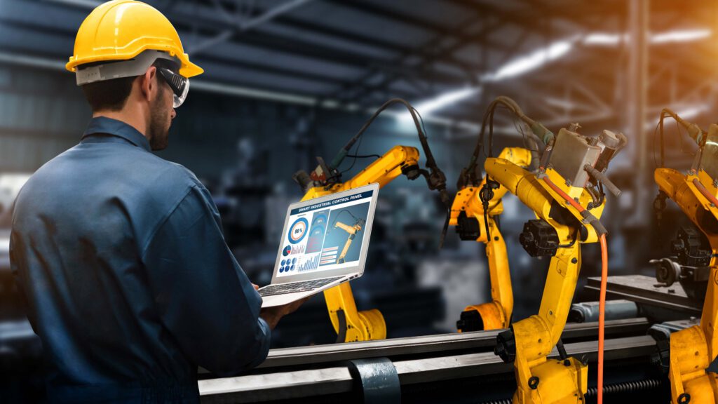Factory worker working on a laptop beside an automated assembly-line
