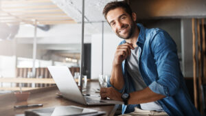 Smiling man in denim shirt using a laptop