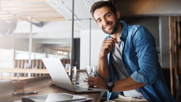 Smiling man in denim shirt using a laptop