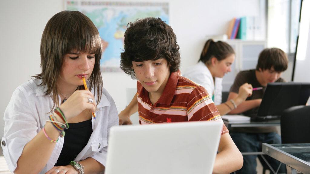 Students in a classroom working on shared laptops
