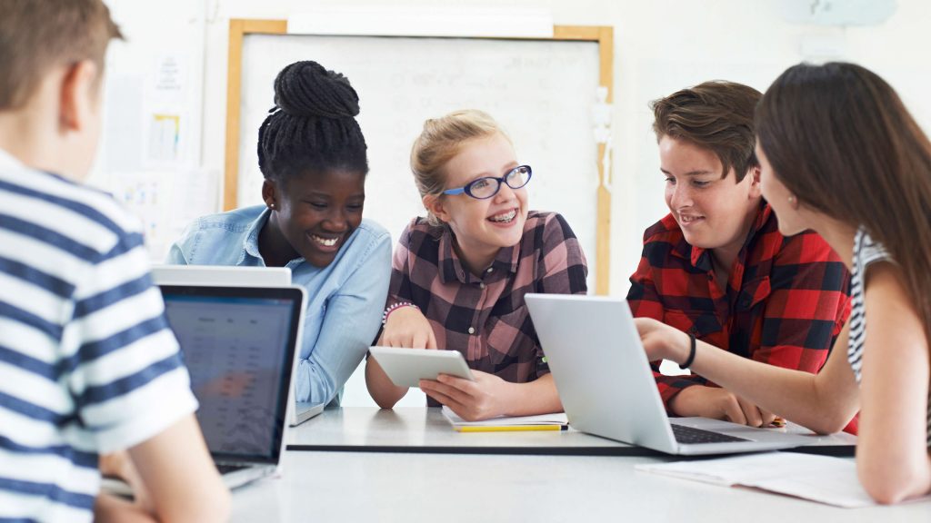 Young teens laughing while working on electronic devices in a classroom